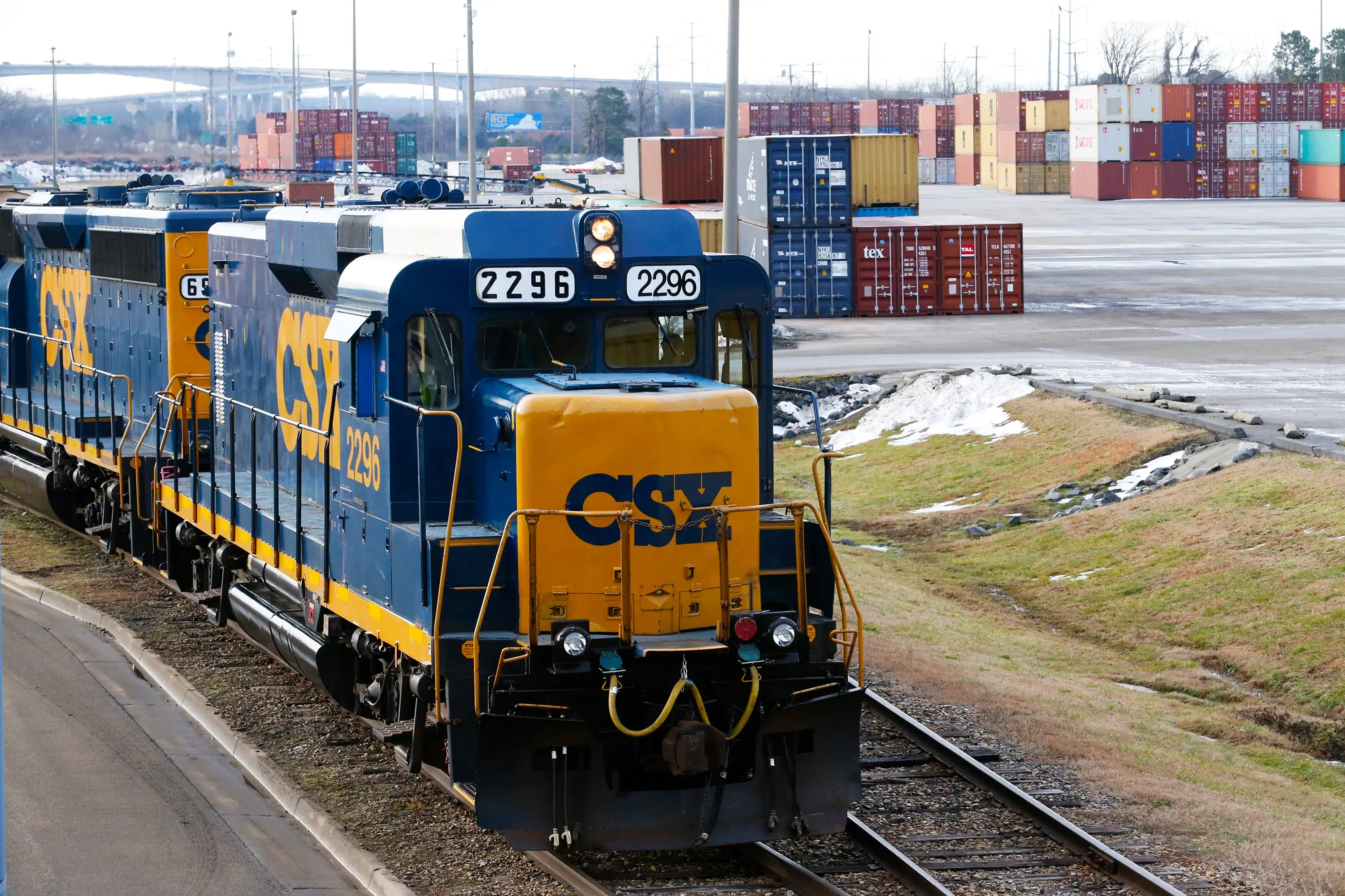 A CSX train on the rail in front of shipping containers